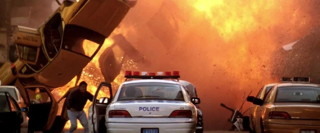 Armageddon (1998) movie still: wide — A chaotic scene shows a yellow vehicle flipping high through the air during an explosion. A man runs away from…