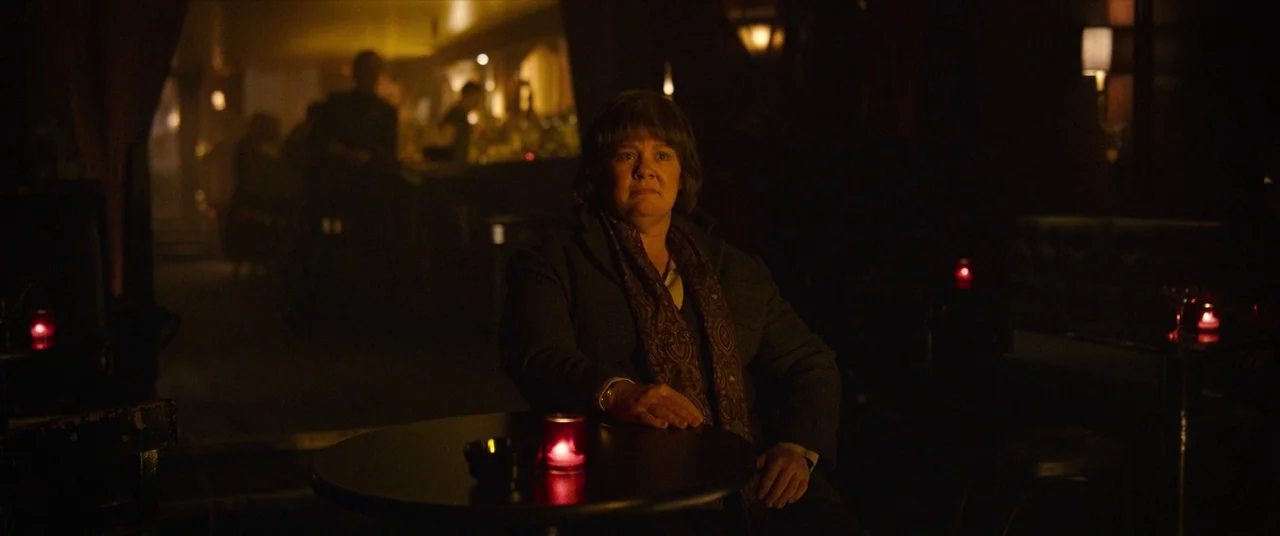 Can You Ever Forgive Me? (2018) movie still: medium — A dimly lit tavern environment features dark booths and obscured figures in the distance. A…