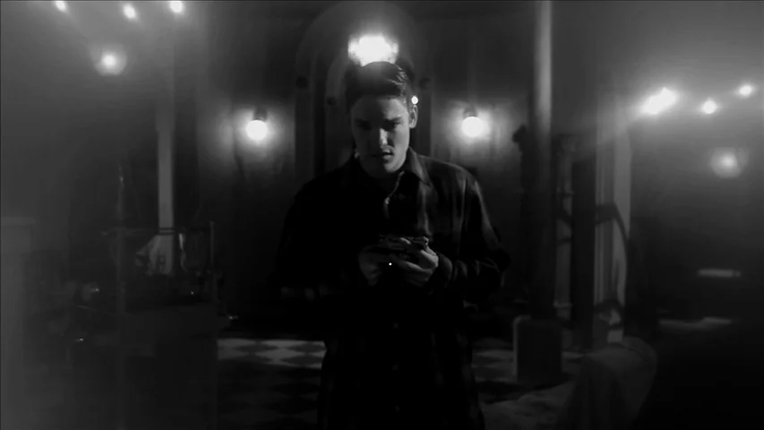 Keyhole (2011) movie still: medium — A dark room with tiled flooring features multiple lit wall sconces and hazy atmosphere. A young man stands in…