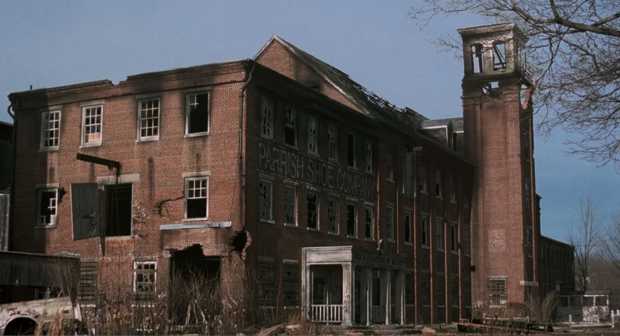 Jumanji (1995) movie still: wide — An abandoned three-story red brick industrial building stands with numerous broken, glassless windows. A tall…