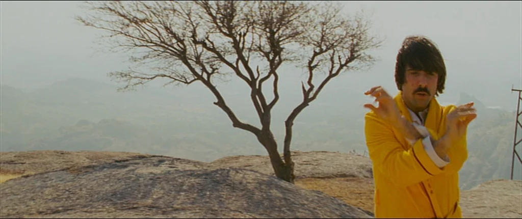The Darjeeling Limited (2007) movie still: medium — A man stands on a rocky plateau overlooking a hazy, distant mountainous landscape. A single…