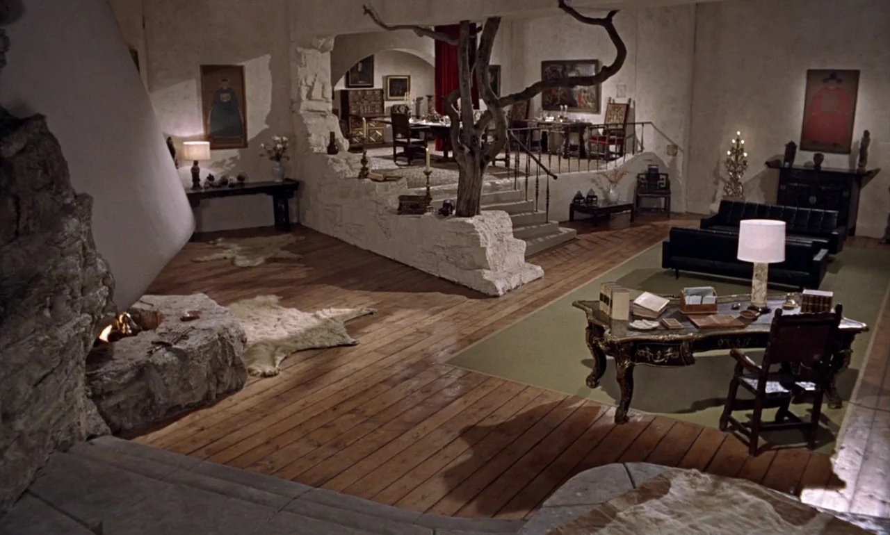 Dr. No (1962) movie still: wide — A split-level room features stone walls, hardwood floors, and a decorative indoor tree. Furnishings include a…