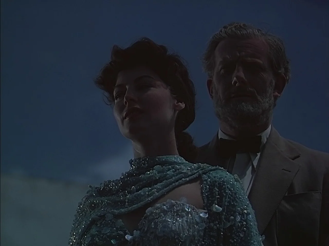 Pandora and the Flying Dutchman (1951) movie still: medium — An outdoor nighttime setting features a man and woman in formal attire. They stand…