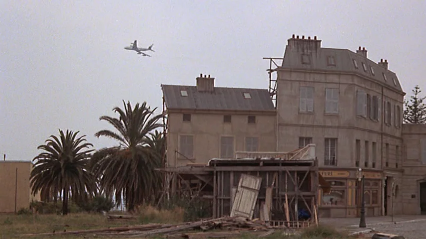 Day for Night (1973) movie still: wide — A stone building with shuttered windows stands next to a wooden construction structure. An airplane is…