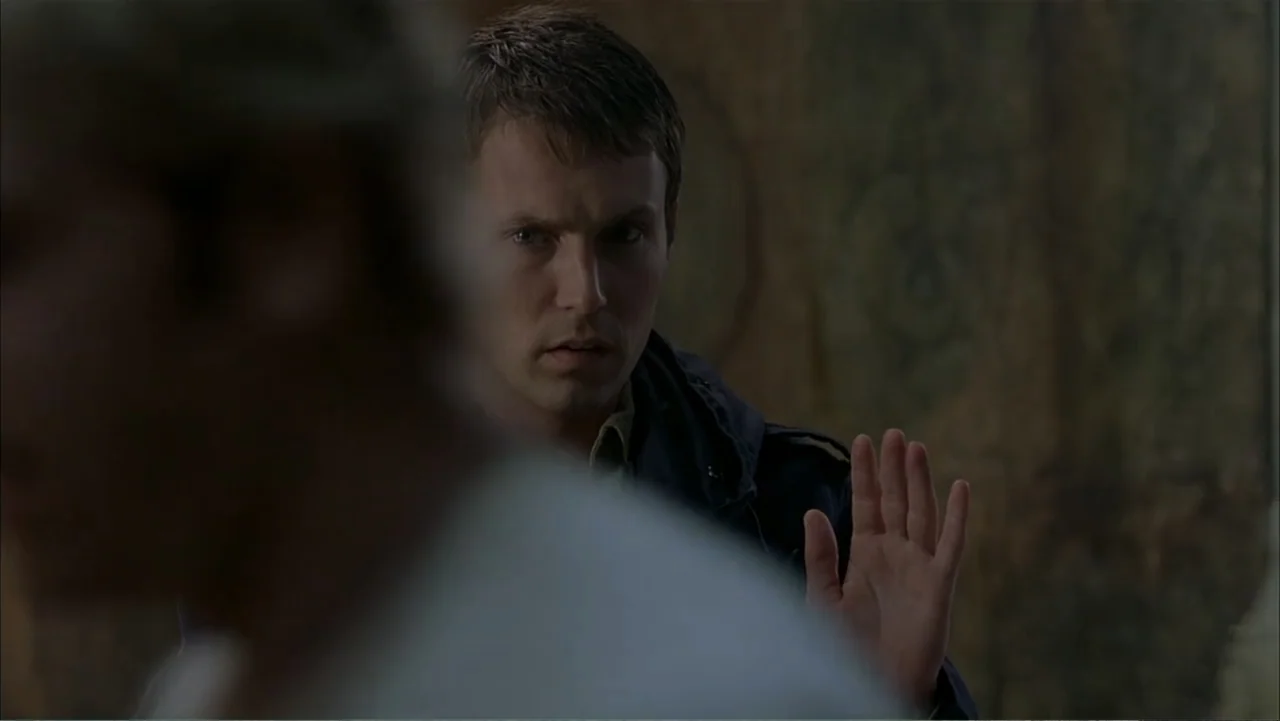 Ghost Ship (2002) movie still: medium — A dimly lit interior space with dark, textured walls providing a shadowy background. A man holds his hand up…