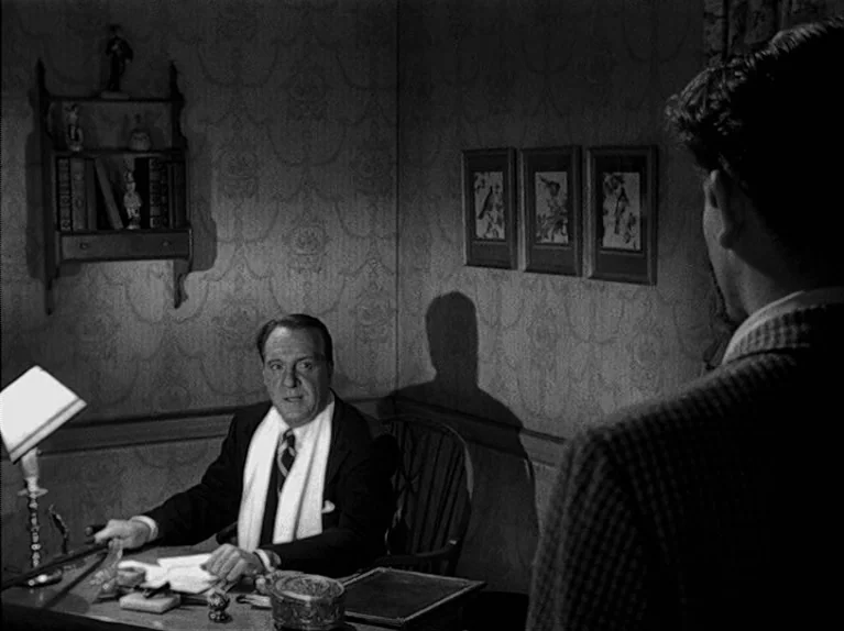 The Big Night (1951) movie still: medium — A man sits at a desk in a room with patterned wallpaper and framed pictures. He looks toward an unseen…