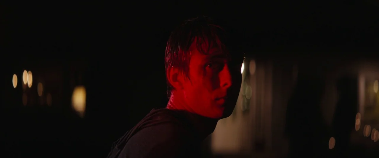 Super Dark Times (2017) movie still: closeup — A dark, blurred outdoor space features distant bokeh lights in the black background. A wet-haired man…