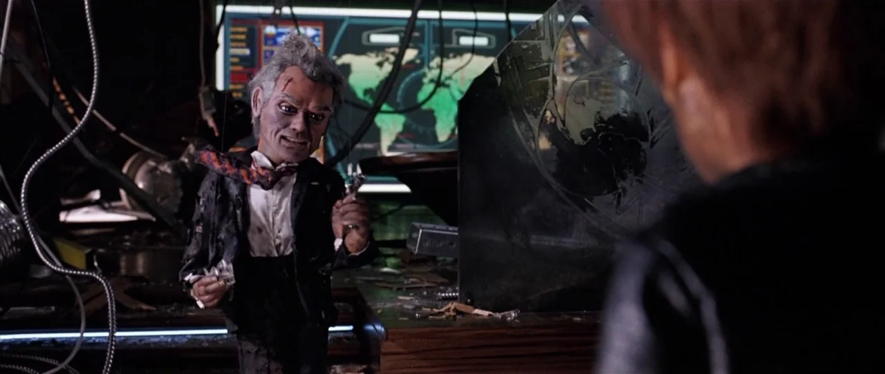 Team America: World Police movie still: medium — A dark command center features a glowing map display on a large screen backdrop. An elderly…