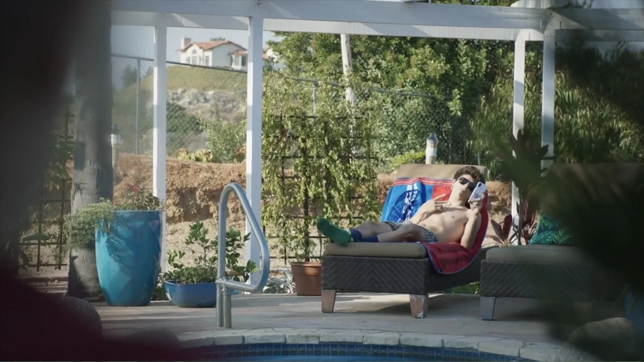 Dos corazones (1919) movie still: medium — A sunny residential patio features a lounge chair beside a tiled swimming pool edge. A teenager in swim…