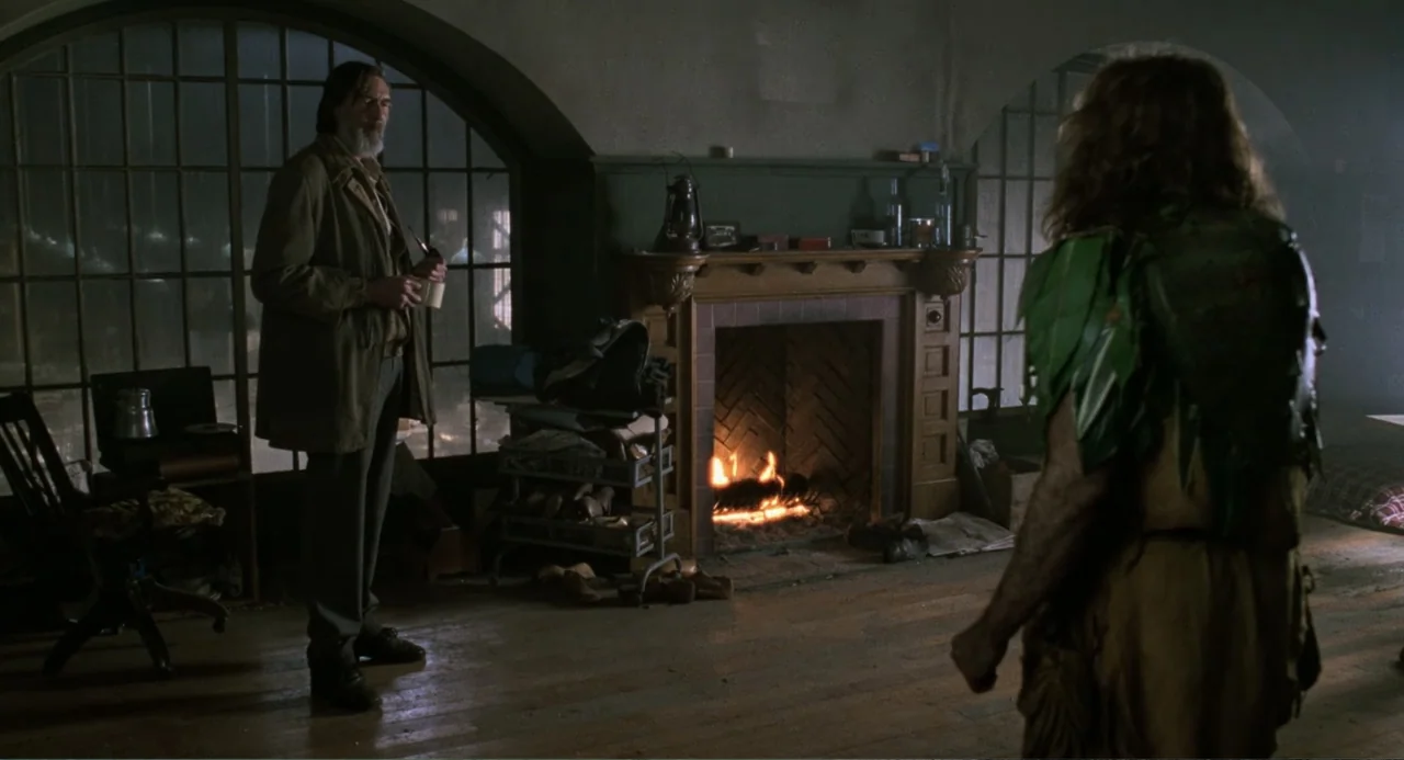 Jumanji (1995) movie still: medium — A rustic cabin interior features a stone fireplace with a fire burning inside it. Two men face each other in a…