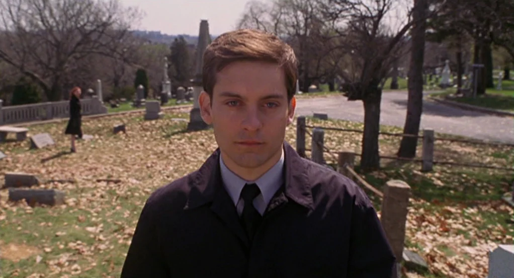 Spider-Man (2002) movie still: medium — An open cemetery with scattered headstones and dry autumn leaves on the ground. A young man stands in the…