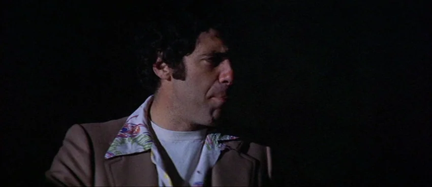 California Split (1974) movie still: medium — A dark, undifferentiated exterior space at night with no visible background environment. A man in a…