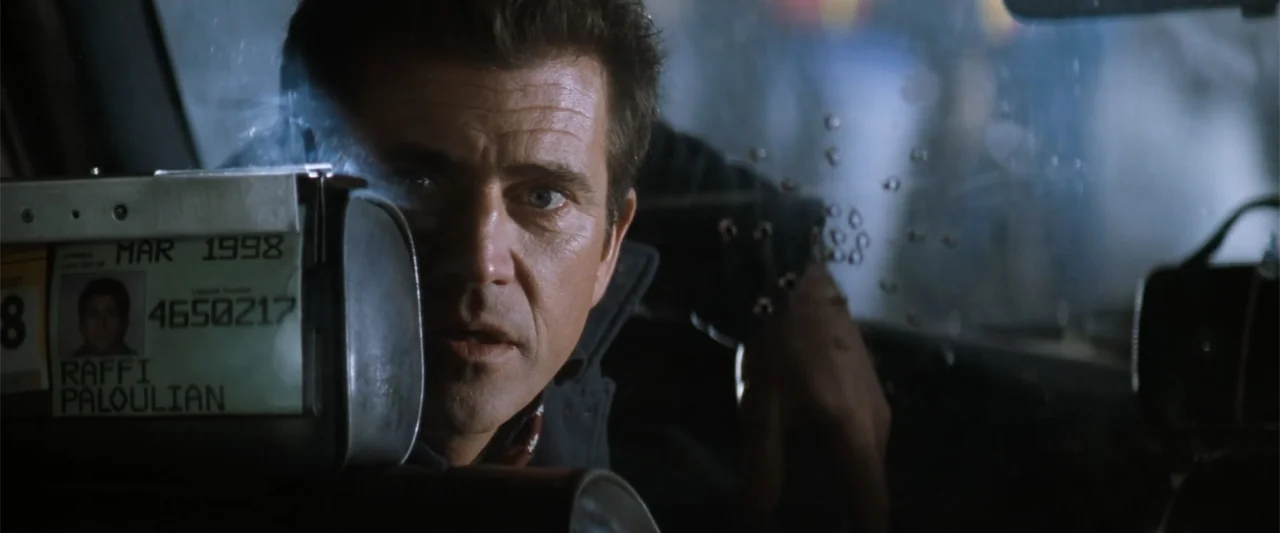 Conspiracy Theory (1997) movie still: closeup — A dark, cramped interior of a taxi cab with a taximeter on the dashboard. A man in his forties…