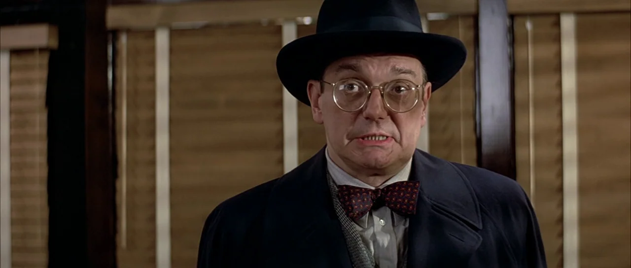 The Untouchables (1987) movie still: medium — An interior space features horizontal wooden blinds in the background behind a man. The man wears a…