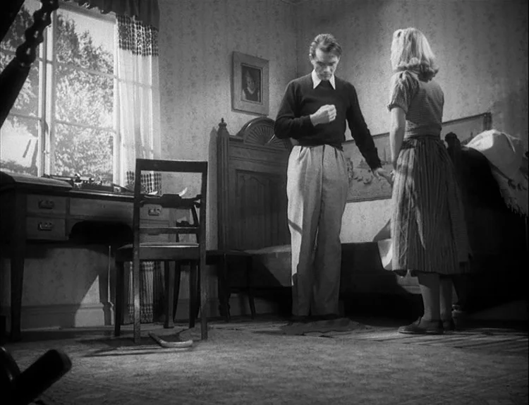 Music in Darkness (1948) movie still: fullbody — A domestic bedroom contains a wooden bed, patterned wallpaper, and a desk by the window. A man…