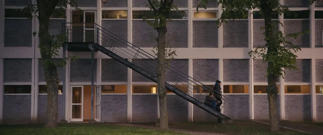 Blue Is The Warmest Colour (2013) movie still: wide — A modern, grey brick school building features a prominent external metal staircase leading…