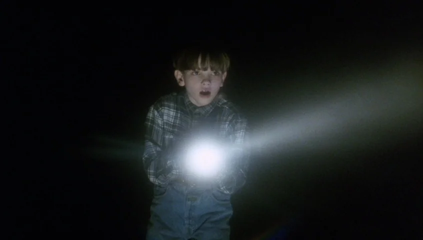 Edward II (1991) movie still: medium — A young boy stands in near-total darkness surrounded by an unidentifiable void. The boy points a bright…