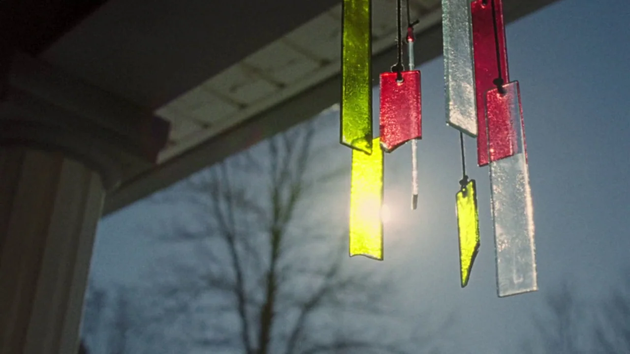 I Am Not a Serial Killer (2016) movie still: closeup — A hanging glass wind chime is suspended from the roof of a house porch. The translucent red,…