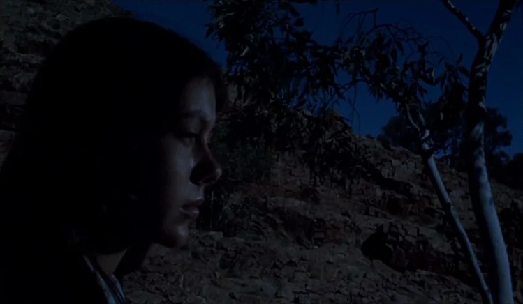 Walkabout (1971) movie still: closeup — A rocky, barren landscape is silhouetted against a dark night sky. A young woman in profile gazes toward the…