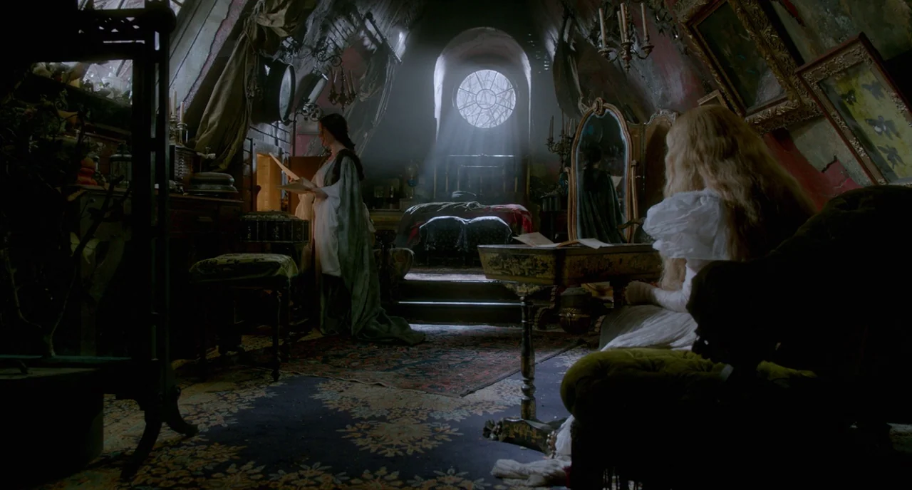Crimson Peak (2015) movie still: medium — A cluttered, moody attic space features vaulted ceilings, ornate frames, and dark vintage furniture. Two…