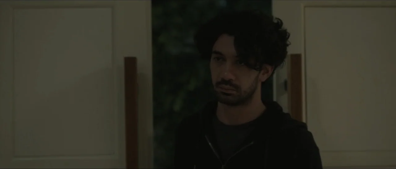 Innocent Vengeance (2023) movie still: medium — A man stands within an interior doorway at night. He is positioned in front of dark foliage visible…
