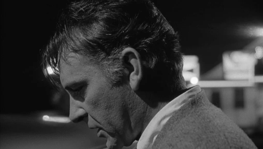 Who’s Afraid Of Virginia Woolf? (1966) movie still: closeup — A man stands in a dark outdoor space at night with blurred buildings visible. The man…