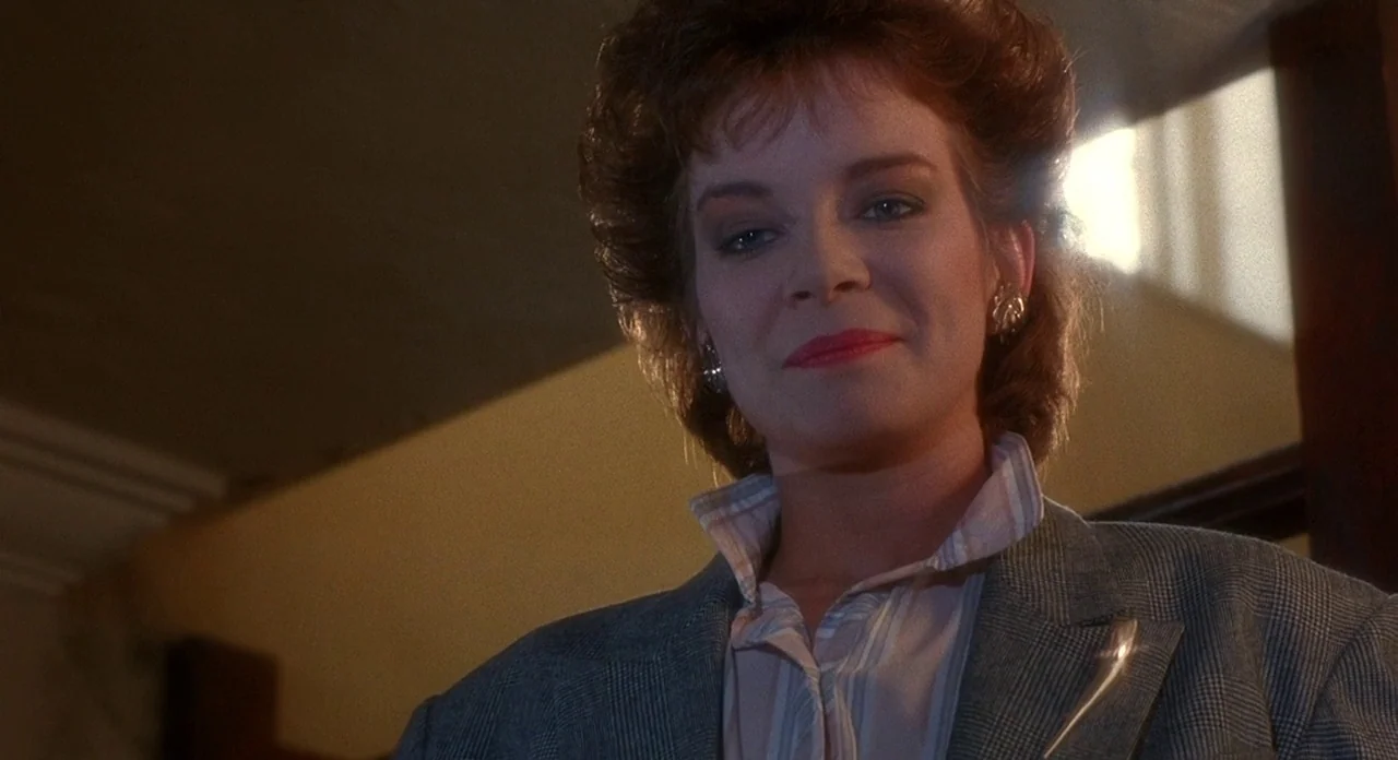Hellraiser (1987) movie still: closeup — A woman stands at the top of a staircase in a house with light walls. She looks down directly into the lens…