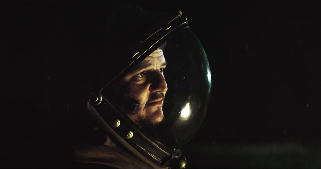 Prospect (2018) movie still: closeup — A person in a spherical helmet sits against a backdrop of complete darkness. The subject turns their head…
