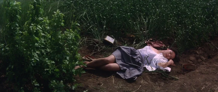 Gate of Flesh (1964) movie still: fullbody — A woman lies on the bare dirt beside a patch of green tall grass. Her body is relaxed as she rests on…