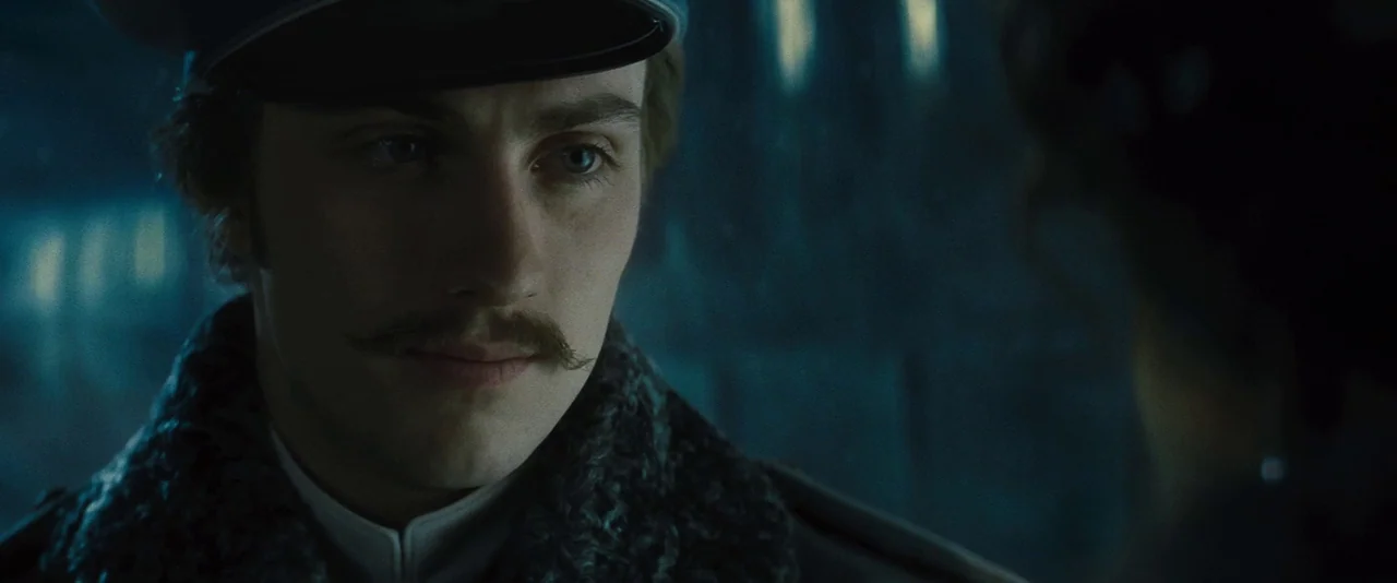 Anna Karenina (2012) movie still: closeup — A dimly lit train carriage features dark textures and shadowy surroundings. A young man in a military…