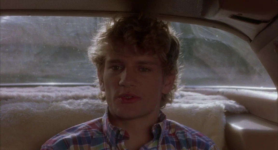 Creepshow 2 (1987) movie still: closeup — The interior of a moving vehicle with a fluffy light-colored seat cover visible. A young man sits in the…