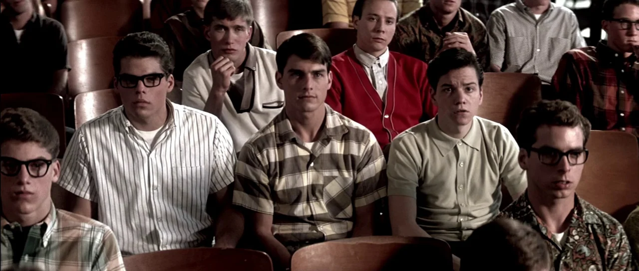 Born On The Fourth of July (1989) movie still: medium — An audience of young men in 1980s clothing sits in curved wooden seats. The men face forward…