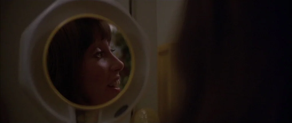 3 Women (1977) movie still: closeup — A dark, dimly lit environment features a person looking into a circular vanity mirror. The woman observes her…