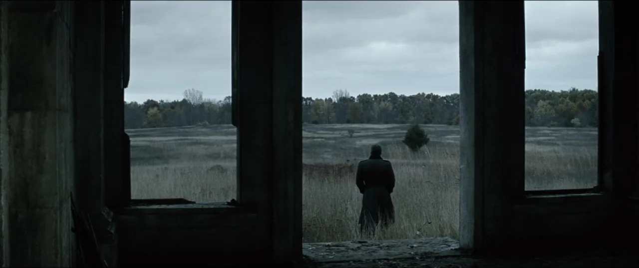 Batman v Superman: Dawn of Justice (2016) movie still: wide — A dark stone interior overlooks a wide open field under a cloudy grey sky. A man in a…