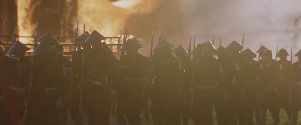 The Last Samurai (2003) movie still: medium — A group of soldiers march through thick smoke with a large fire in background. The men are dressed in…