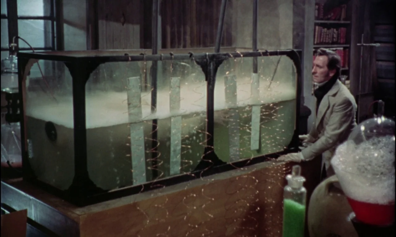 The Curse of Frankenstein (1957) movie still: medium — A dimly lit scientific space features a large dual-chambered glass tank with bubbling liquid.…
