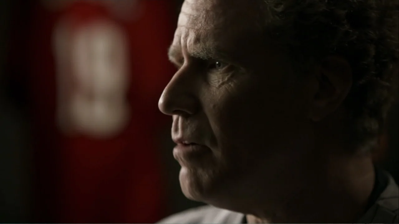 Ferrell Takes the Field (2015) movie still: closeup — A dark indoor locker room contains a man in the foreground. The man looks off-screen while…