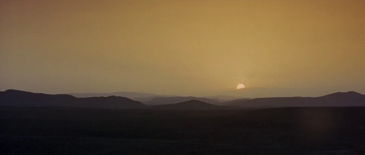 The Hills Have Eyes (2006) movie still: establishing — An arid desert landscape features layers of dark hills silhouetted against a golden sky. The…