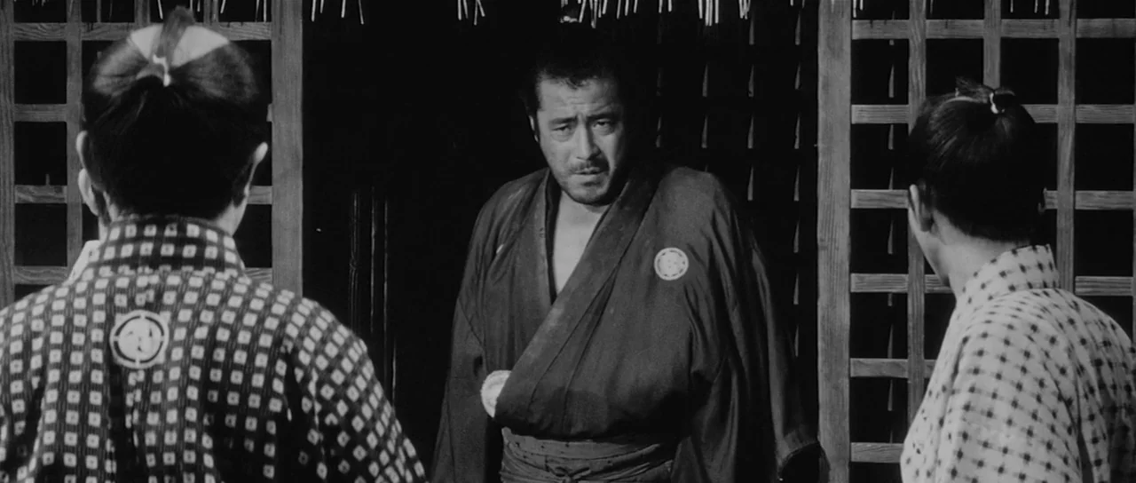Sanjuro (1962) movie still: medium — A traditional room features dark wooden lattice walls and shadowed corners. A man stands between two people as…