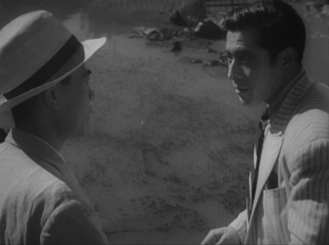 Drunken Angel (1948) movie still: medium — Two men talk while standing on a sand surface near the shoreline. The setting appears to be a sandy beach…