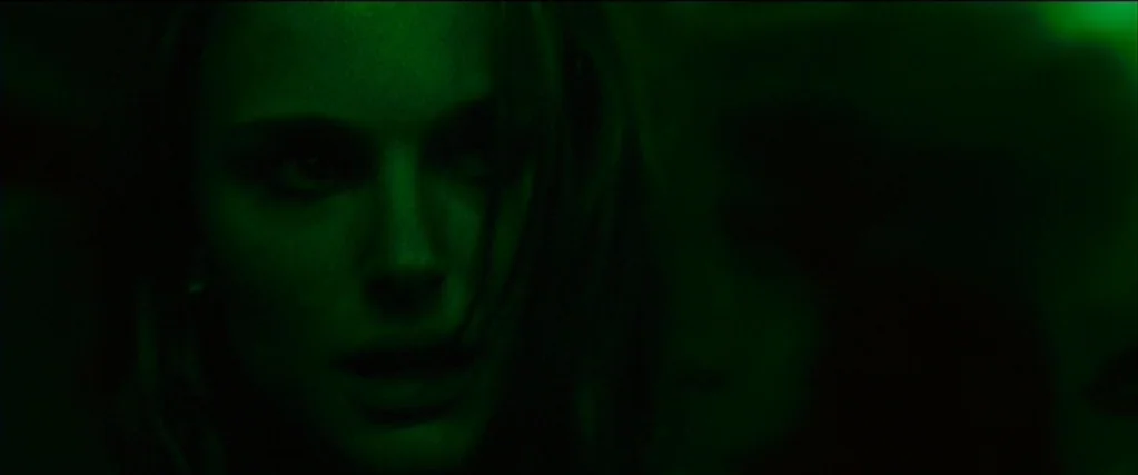 Black Swan (2010) movie still: closeup — A dark, indistinct space is engulfed in saturated green light. A woman's face emerges from the shadows, her…
