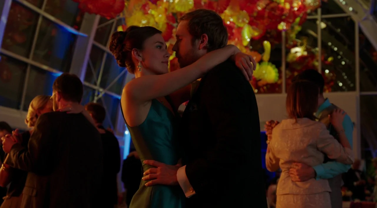 Laggies (2014) movie still: medium — A dark ballroom filled with people dancing under large clusters of glowing orange sculptures. A couple in…