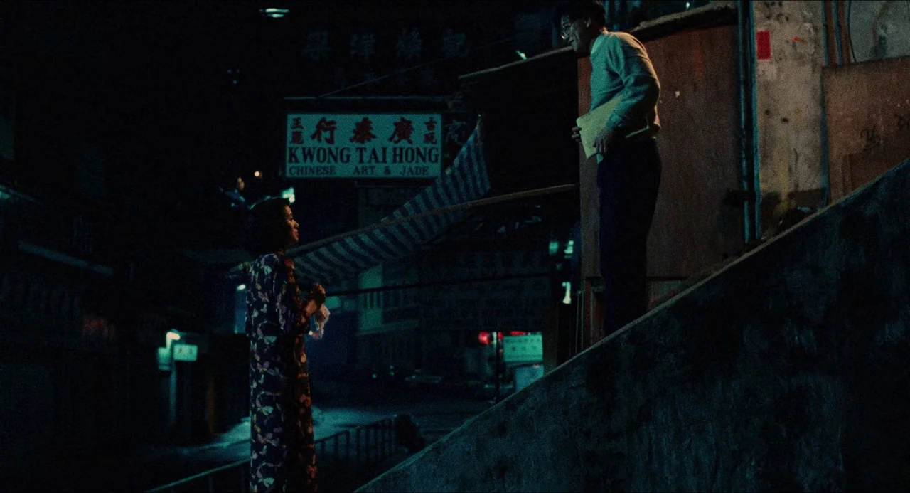 Rouge (1987) movie still: wide — A dark urban staircase at night with a prominent neon sign in the background. A man stands on the top step facing a…