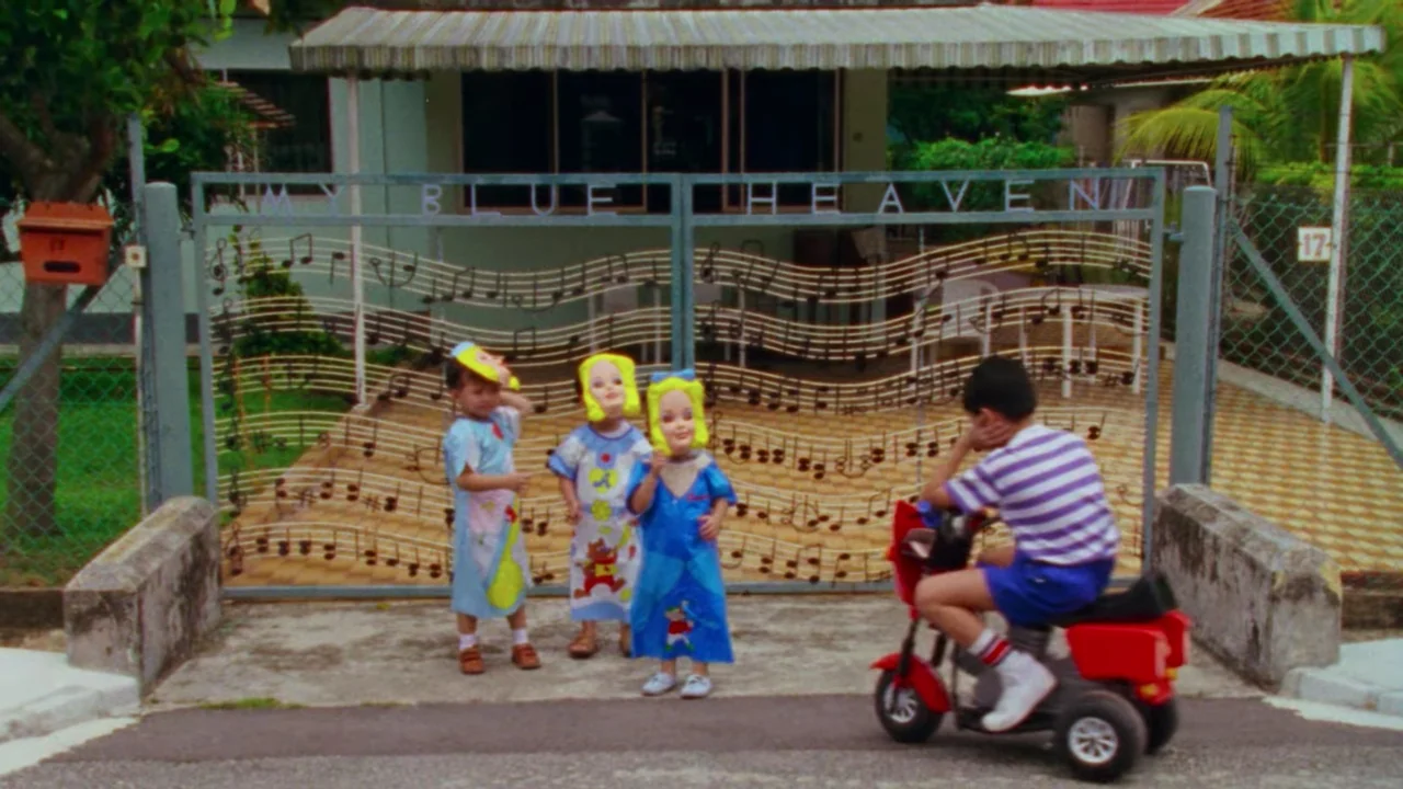 Shirkers (2018) movie still: wide — A residential house gate features a unique musical staff design with notes welded across. Three children stand…