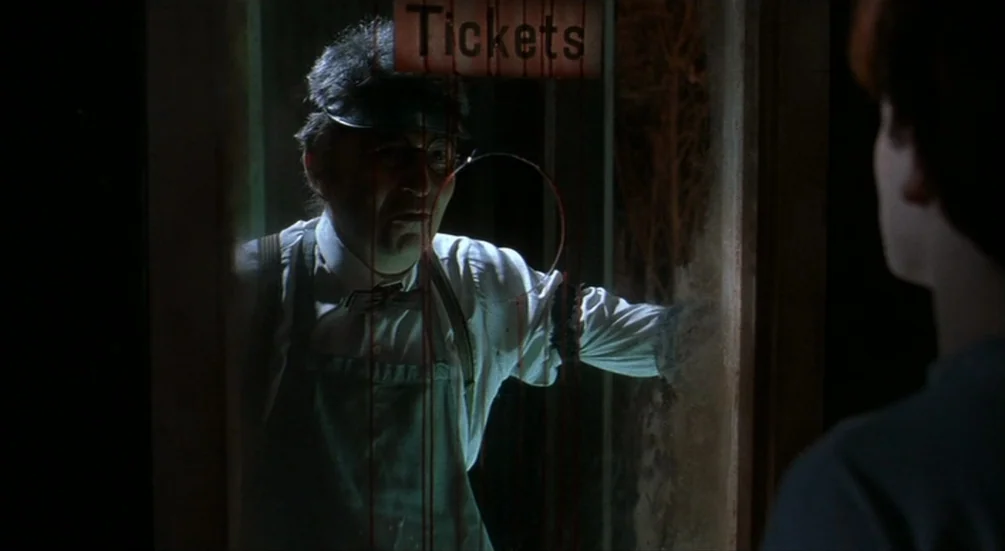 Freddy’s Dead: The Final Nightmare (1991) movie still: medium — An older man operates a small, dimly lit ticket booth with glass partitions. He…