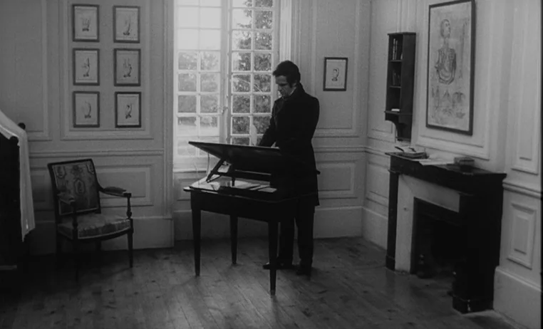 The Wild Child (1970) movie still: fullbody — A room with wood flooring, framed prints on the walls, and a fireplace mantel. A man in a dark coat…