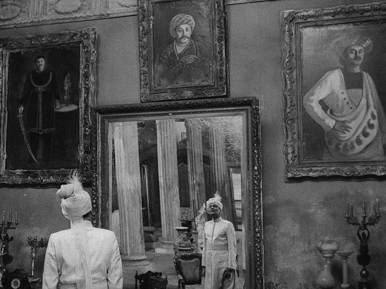 The Music Room (1958) movie still: medium — An opulent room features a large mirror framed by three historical oil paintings. A man stands with his…