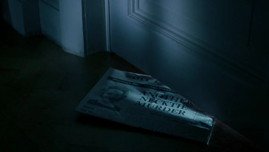 Frenzy (1972) movie still: closeup — A newspaper with a bold headline lies on a wooden hallway floor. The paper rests against the base of a closed…