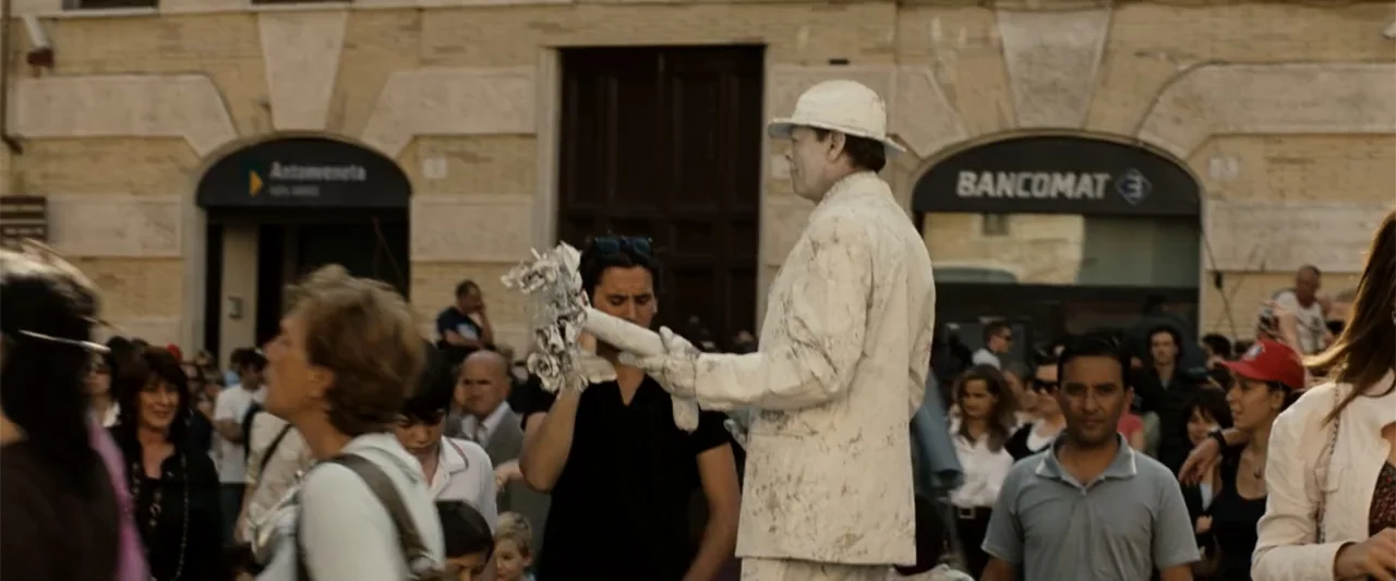 Angels & Demons (2009) movie still: medium — A crowded public plaza with stone buildings featuring large arched doorways in the background. A street…