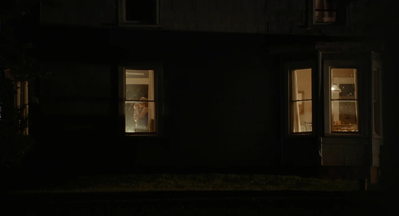Bones and All (2022) movie still: wide — A dark, two-story house exterior is visible at night against a pitch black sky. Warm light shines through…